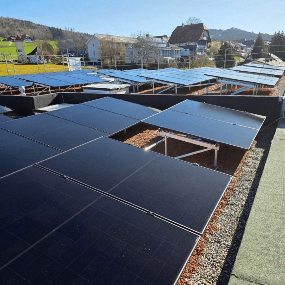 Solar panels installed on a flat rooftop with a village and hills in the distance on a sunny day.