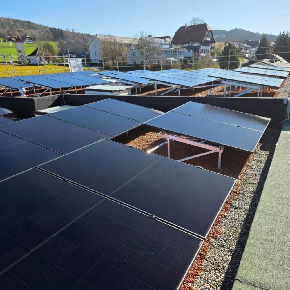 Solar panels installed on a flat rooftop with a village and hills in the distance on a sunny day.