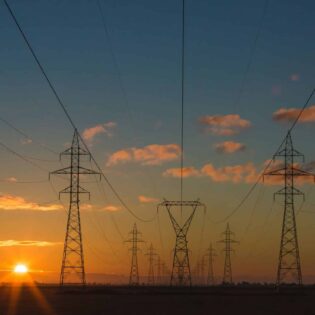 Energiebranche-Stromleitungen-Stromsystem-PV für Regelenergie Transmission towers and power lines silhouetted against a sunset sky, creating a network of cables across the horizon.
