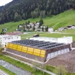 KI-generierte Visualisierung der PV- und Fassadenanlage auf Sporthalle Färbi in Davos. Die Anlage wird in den üblichen dunklen Farben gebaut.