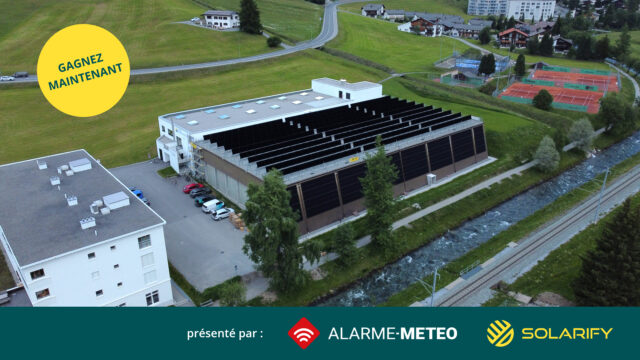 Aerial view of a solar-panel building beside a river and green hills, with a road and tennis courts in the background; a large yellow circle reads 'GAGNEZ MAINTENANT' over the scene.