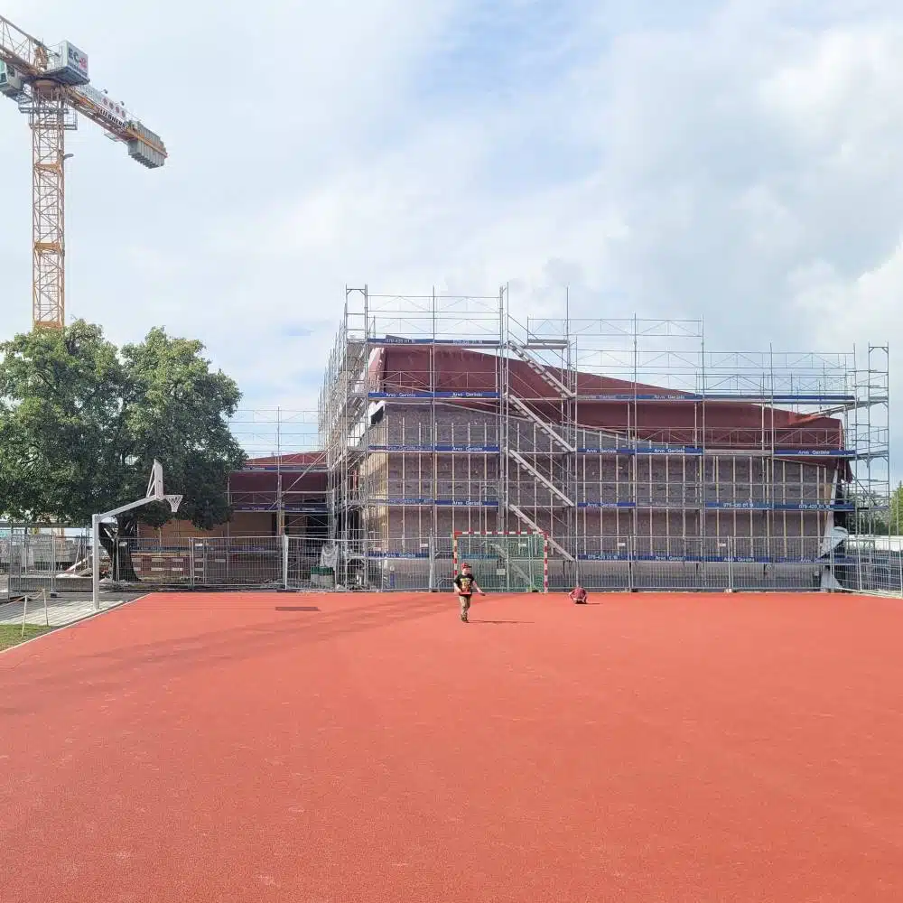 Blick vom Sportplatz auf das neue Gebäude mit Gerüst der Turnhalle in Adetswil